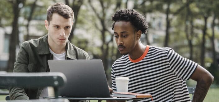 Focused young diverse men working online on laptop in park