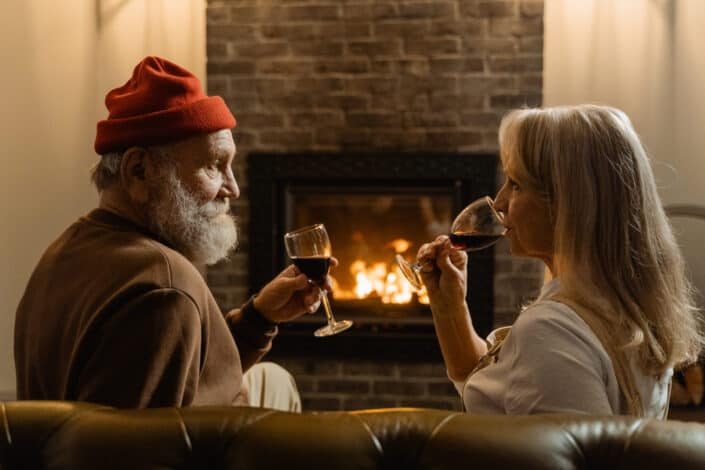 Old couple drinking wine by the fireplace