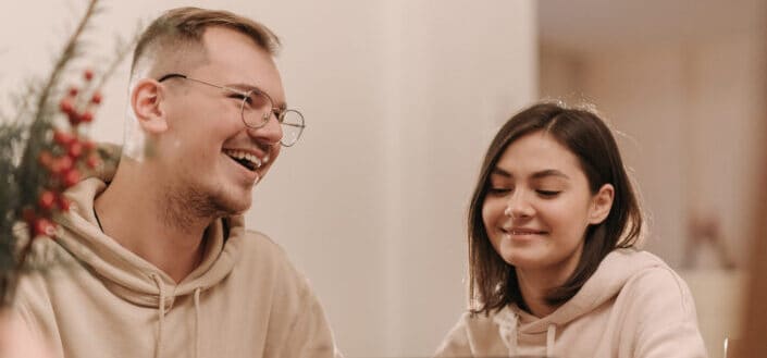 Man and woman in beige hoodie laughing in front of an ipad