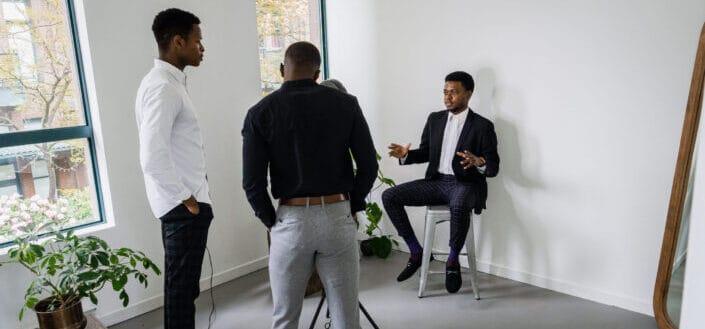 Man in a suit sitting on a gray stool