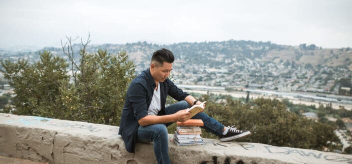 Man in black long sleeves and denim jeans reading a book