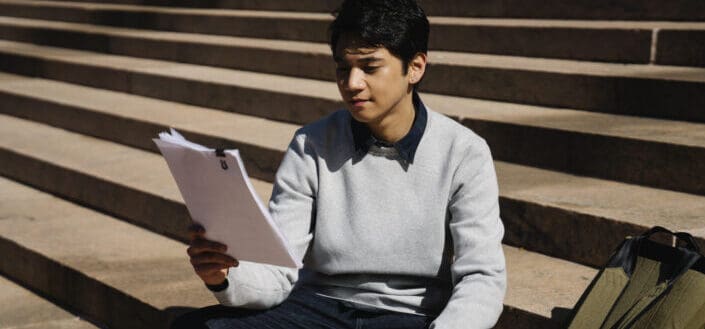 Man in gray sweater reading while sitting on concrete stairs