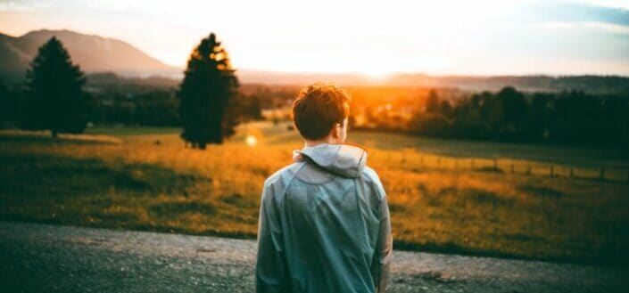 Man standing beside road facing sun