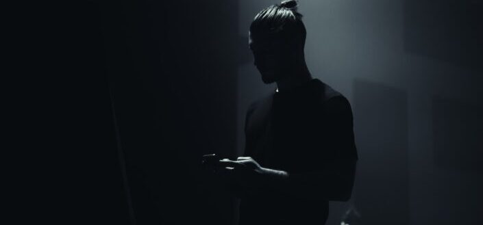 Guy standing in a dark room while holding his phone
