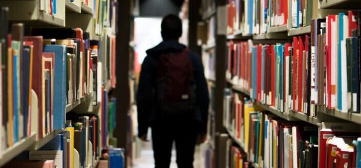 man with backpack beside a books