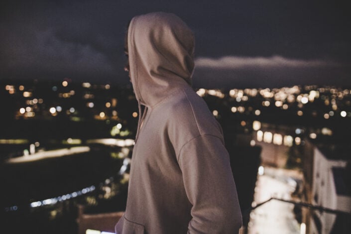 Person in gray pullover hoodie looking over the night view of a city