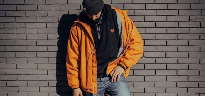 A man in a casual attire standing outside leaning against a bricked wall
