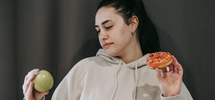 Thoughtful woman choosing between green apple and donut