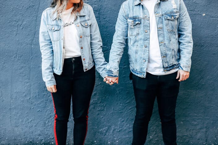 Two person standing and holding their hands beside blue wall