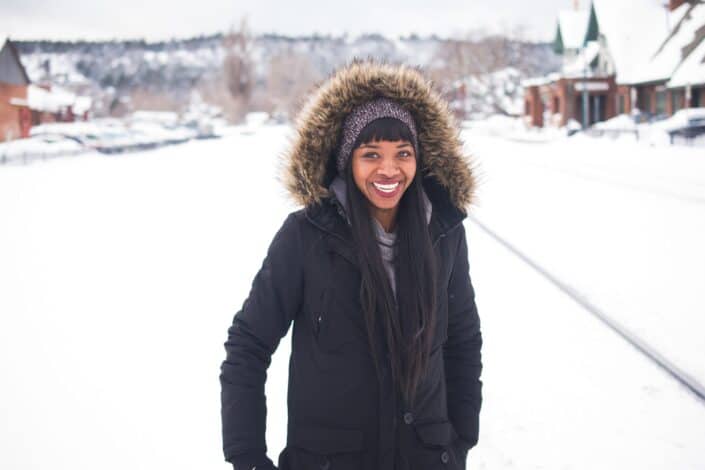 Woman wearing coat standing outside smiling while enjoying the white thick snow