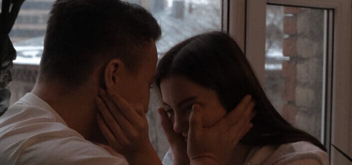 Young couple touching each others face tenderly on windowsill