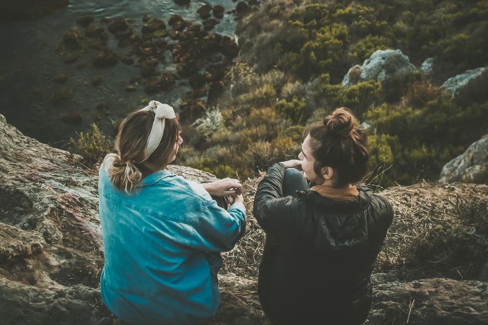 two women sitting on cliff while chatting