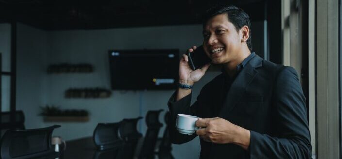 Smiling man holding cup and using smartphone