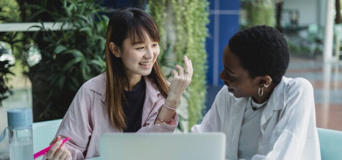 Smiling students interacting at table with laptop