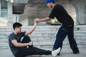 Asian man helping friend to get up from ground - featured