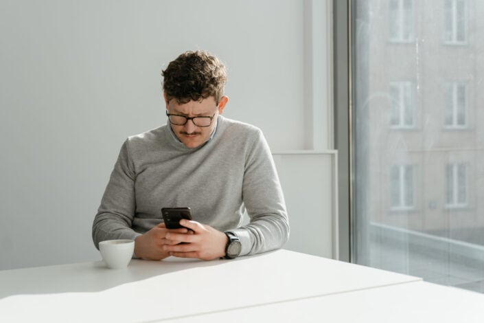 A Man in Gray Sweater Using His Phone