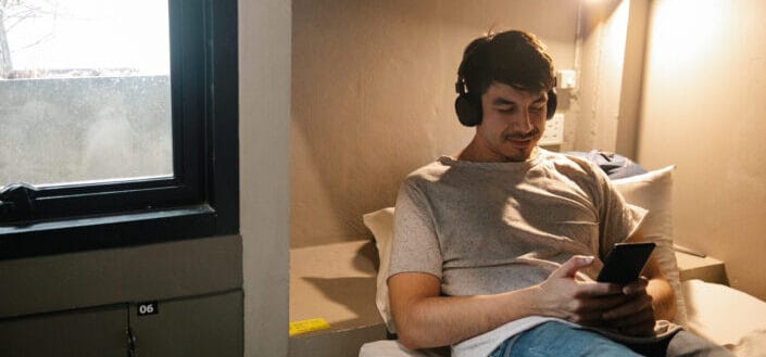 Smiling Man Resting on Bed and Using Smartphone and Headphones