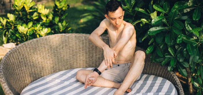 Shirtless Man Sitting and Putting on Sunscreen