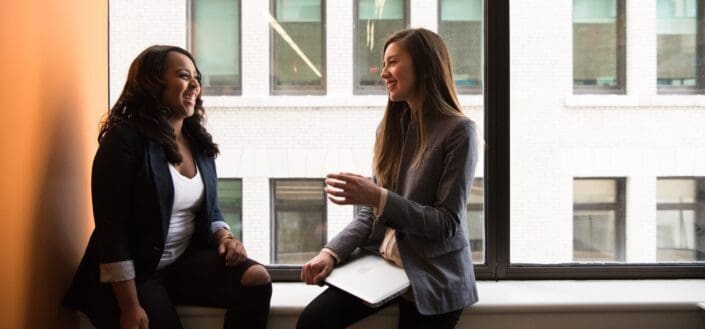 two woman sitting by the window laughing