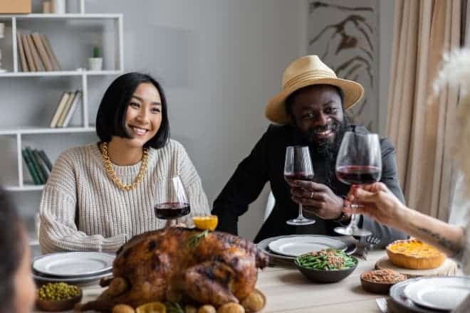 positive multiethnic couple drinking wine with guest - Best Thanksgiving Jokes