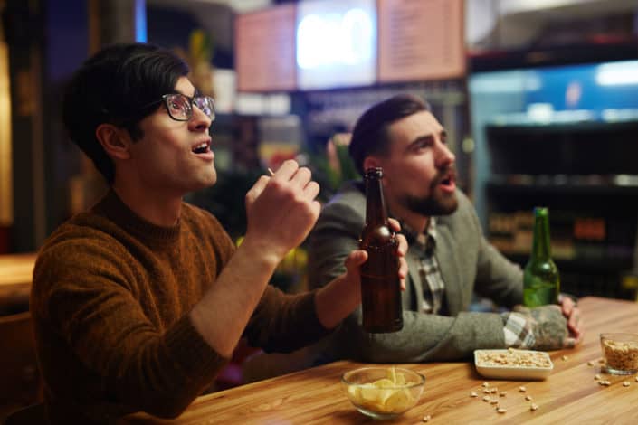 Two guys, drinking beer, reacting on something interesting.