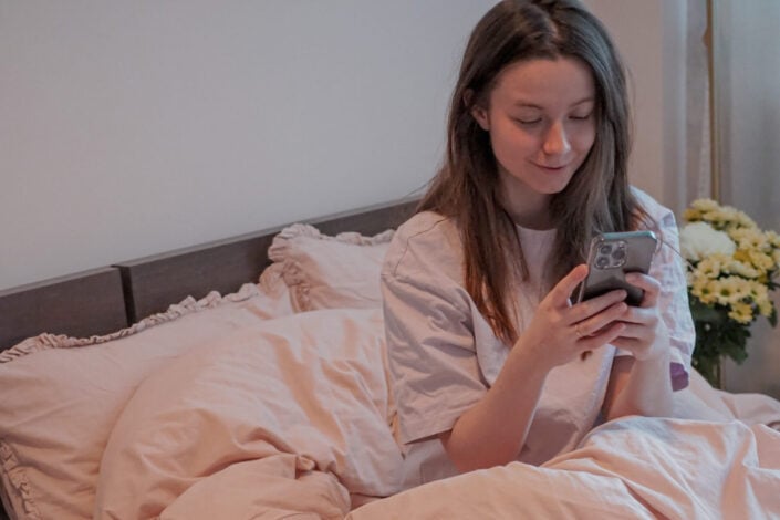woman sitting in bed holding a cellphone