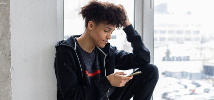 man sitting on windowsill and using smartphone