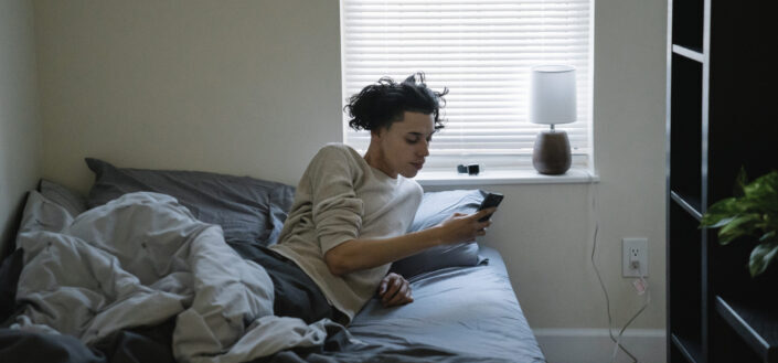 man chatting on smartphone in bed at home