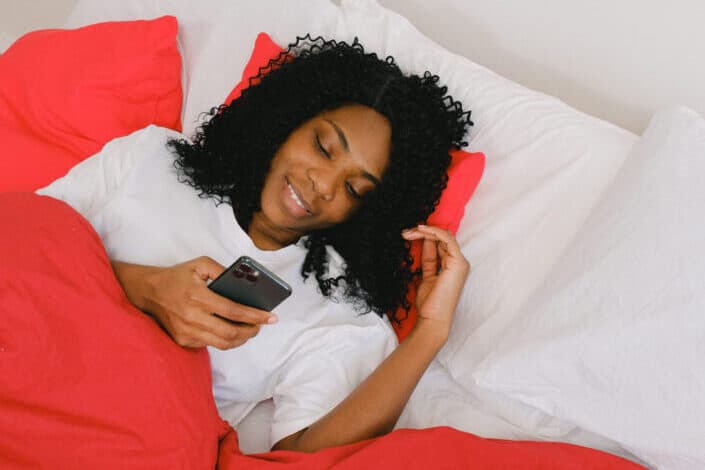 Happy woman using smartphone under blanket