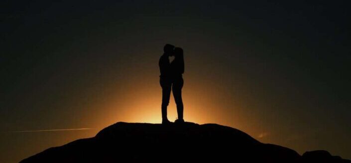 Couple standing on a sunset hilltop kissing