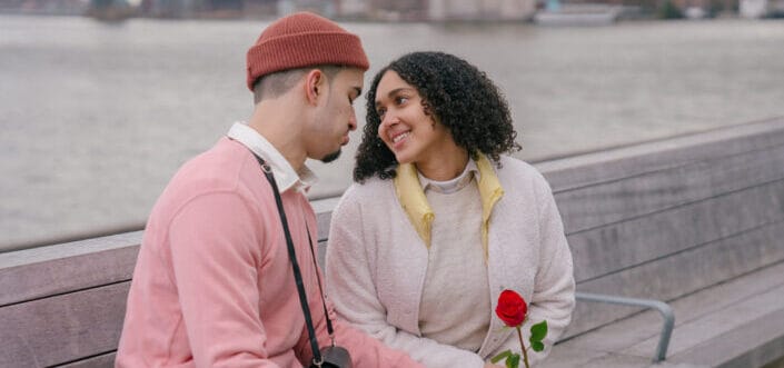 Hispanic couple with rose sitting on embankment