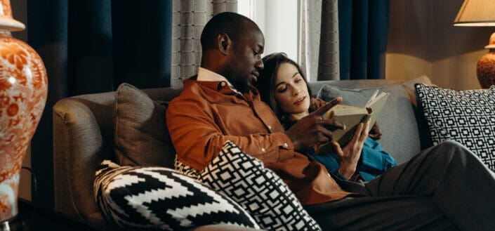 Couple Sitting on Couch While Reading a Book