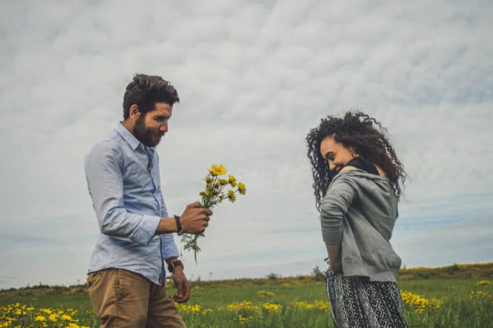 Man giving a shy woman freshly picked yellow flowers