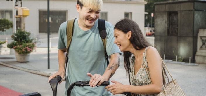 Cheerful multiethnic couple laughing and carrying bicycle
