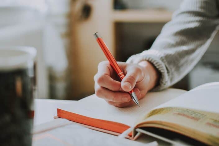 person writing in notebook with red pen