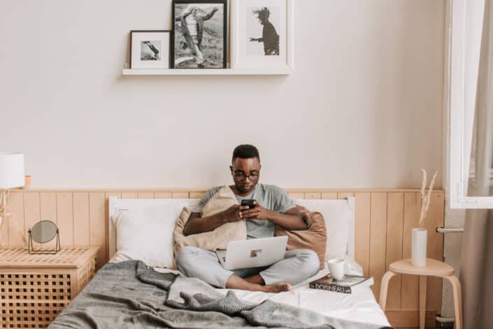 man sitting on bed while using cellphone