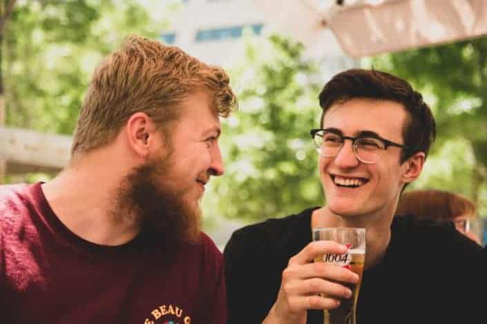 two men smiling at each other, the other holding a glass of beer