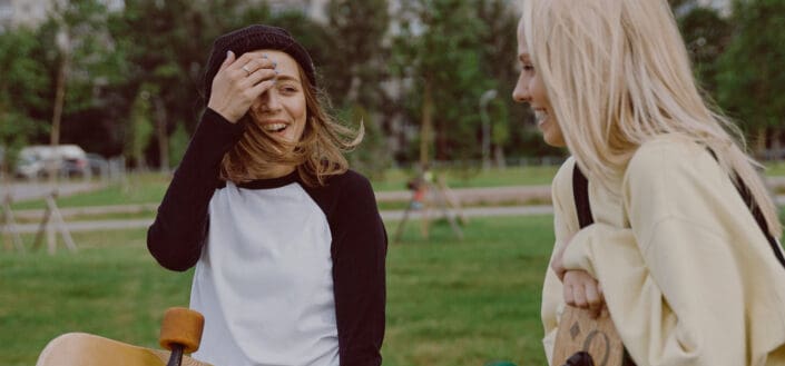 Women Holding Longboards at a Park Having a Chat