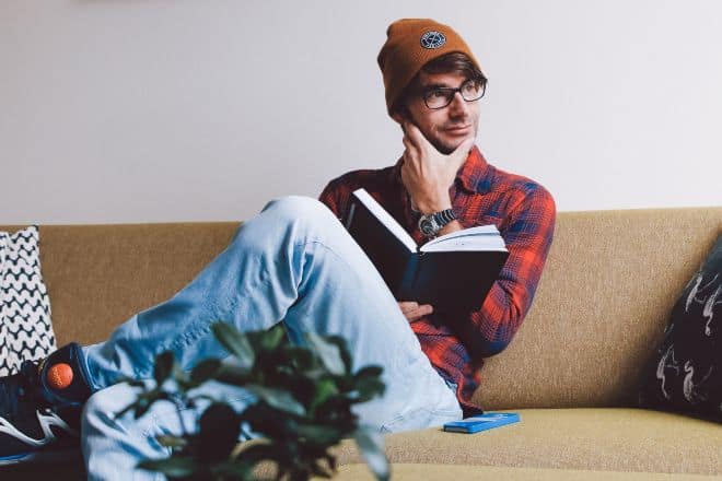 Man sitting on sofa while holding book - What Am I Riddles
