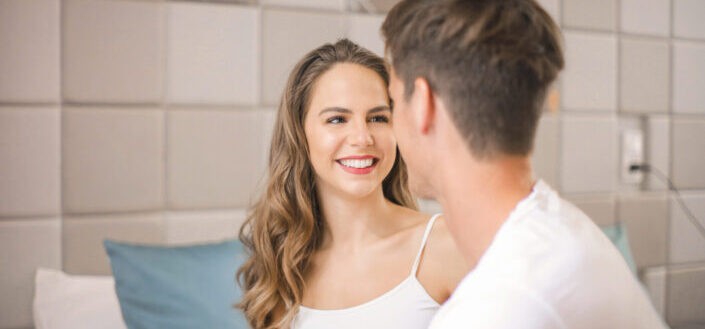 Woman smiling beside man in bedroom