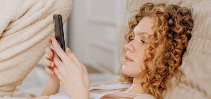 Woman lying on bed holding smartphone