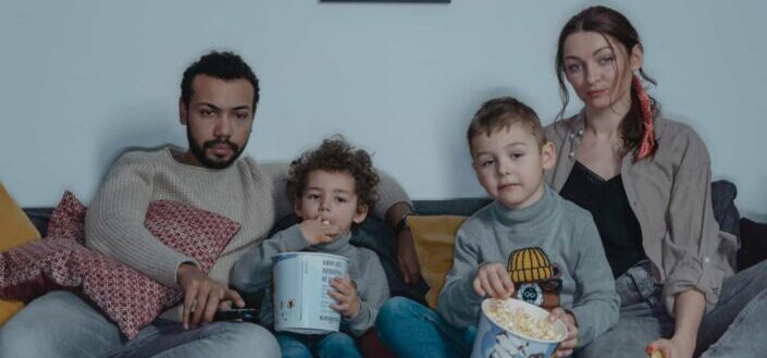 Family sitting on blue sofa eating popcorn