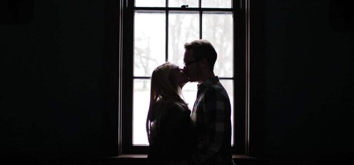 Man and Woman Kissing Beside a Window