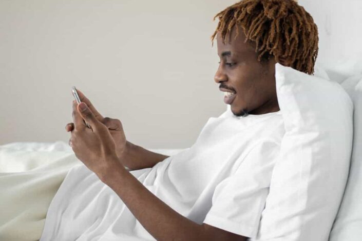 Man in white shirt using phone in bed