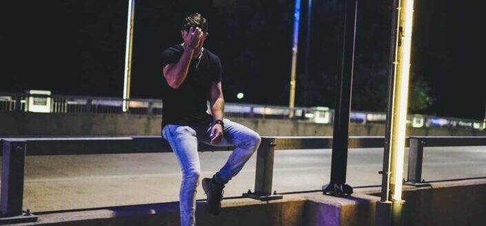 man sitting on bridge railing at night