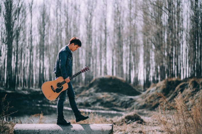 Man with acoustic guitar walking in forest
