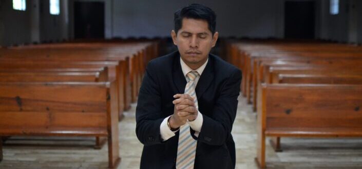 man wearing black suit while praying