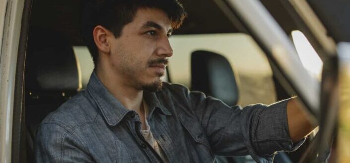 Serious young guy driving car at sundown