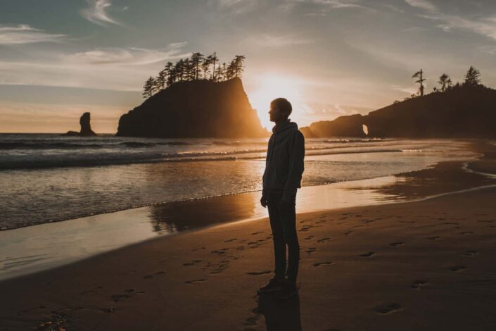 man standing on seashore during sunset