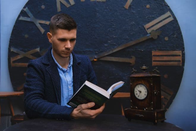 man reading book next to clocks - Theta Male